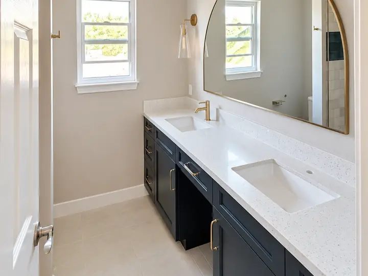 Bathroom vanity cabinets painted deep navy with brass pulls under a white quartz counter