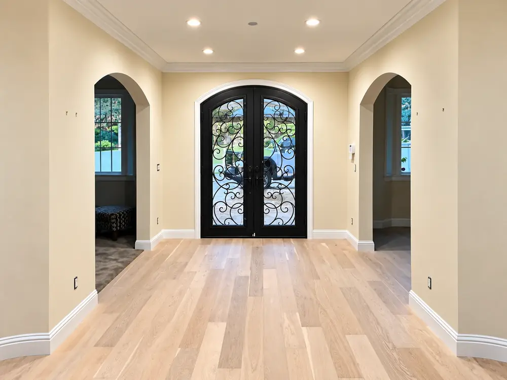 Entry hall with warm cream walls, white crown molding and arched doorways around a black iron door