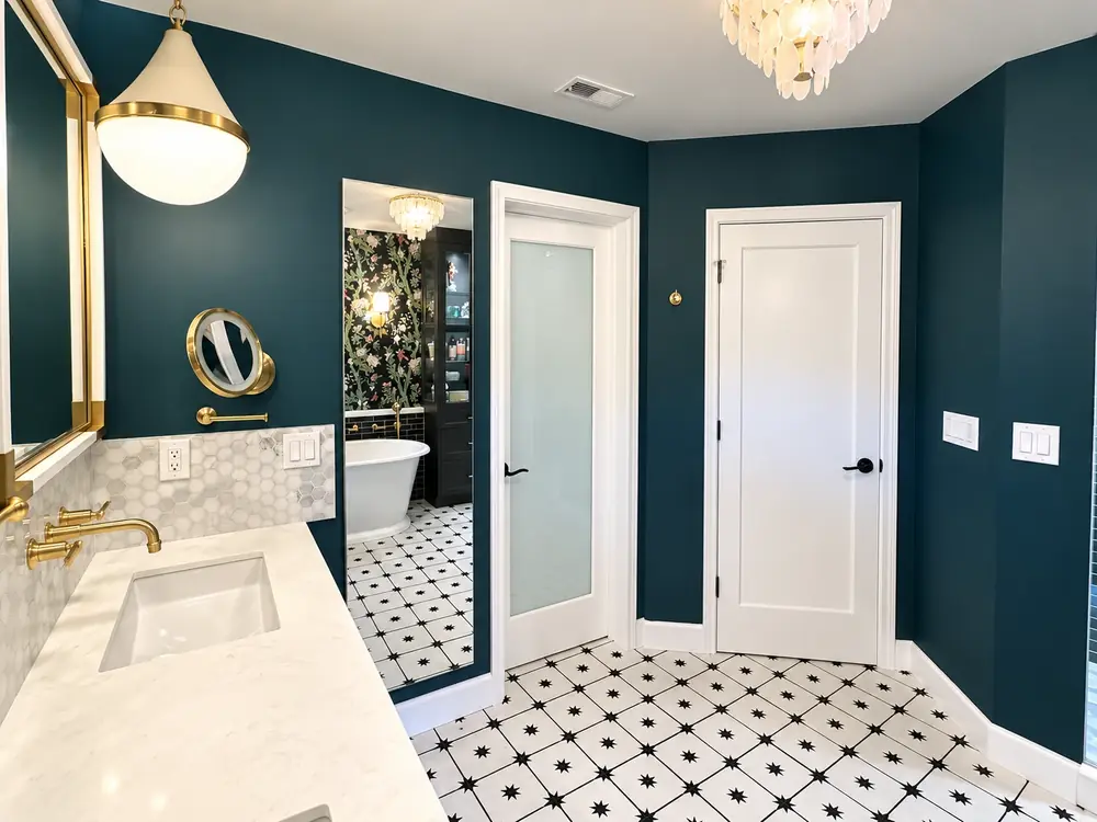 Bathroom with deep teal painted walls, white doors and trim and brass fixtures