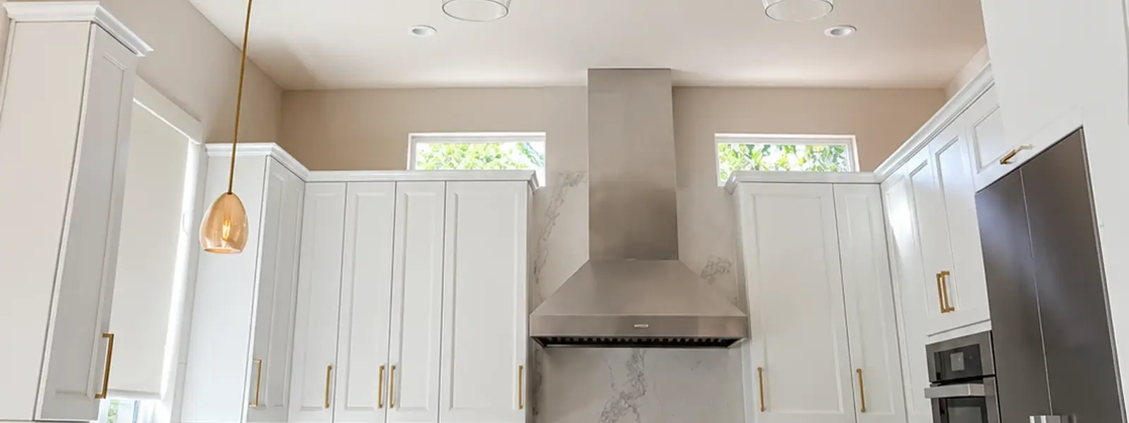 White painted kitchen cabinets with gold pulls, a marble backsplash and a stainless hood